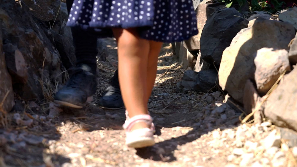 Ett barn i sandaler och klänning går på en grusstig på den grekiska ön Lesbos, endast benen syns.