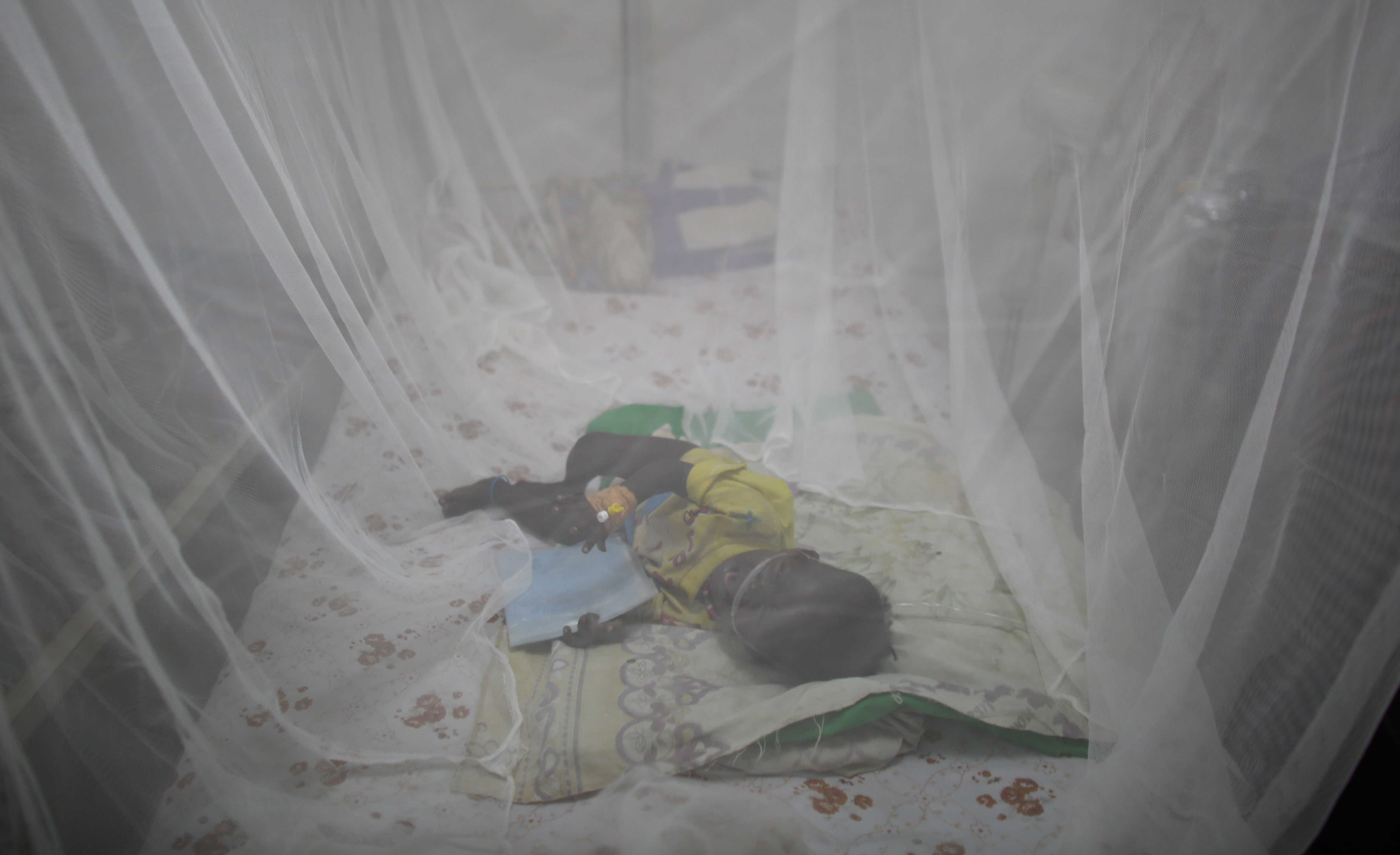 Ett barn ligger under ett myggnät på en säng i Sydsudan.