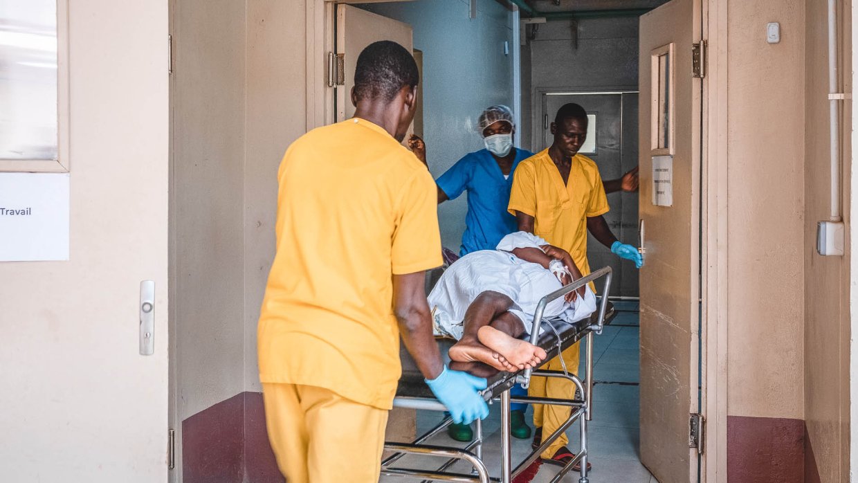 En kvinna liggandes på en sjukhussäng förs in till ett annat rum av tre personer i sjukvårdskläder.