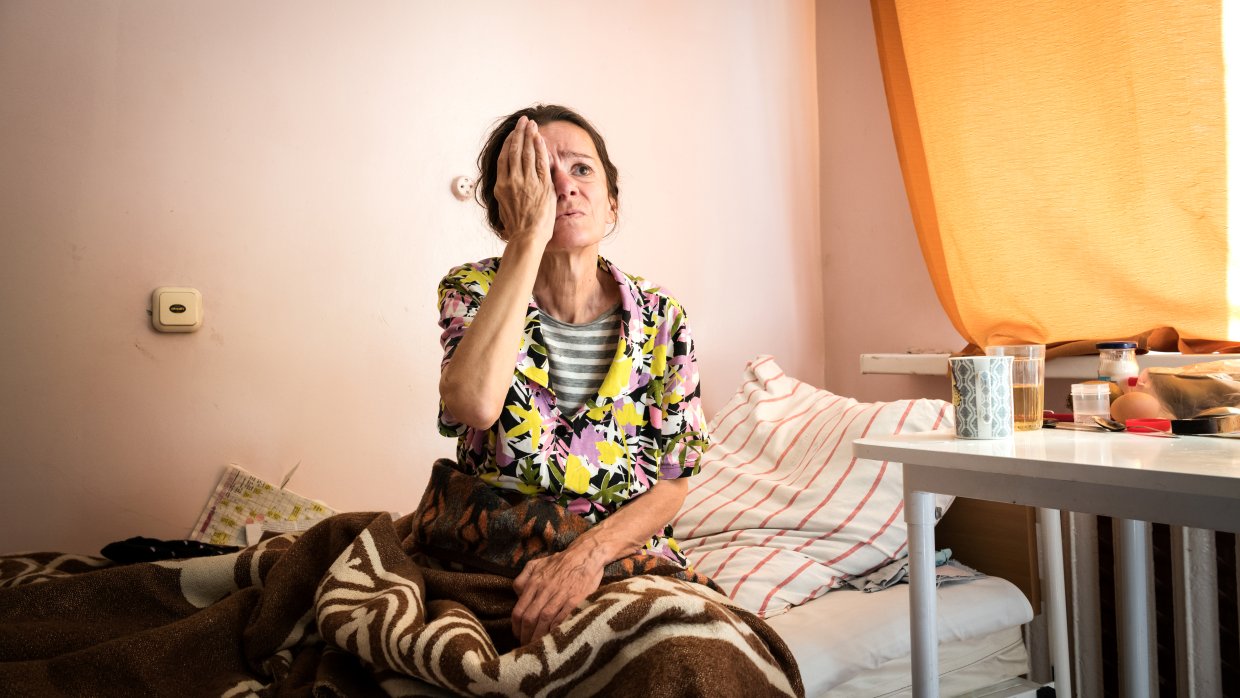 en kvinna sitter på en sjukhussäng och håller för ena ögat för ett syntest