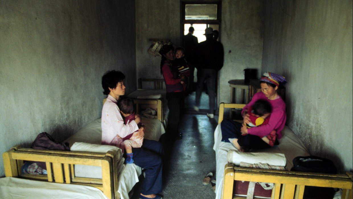 två kvinnor sitter med små barn i famnen på ett par sängar i ett sjukhusrum