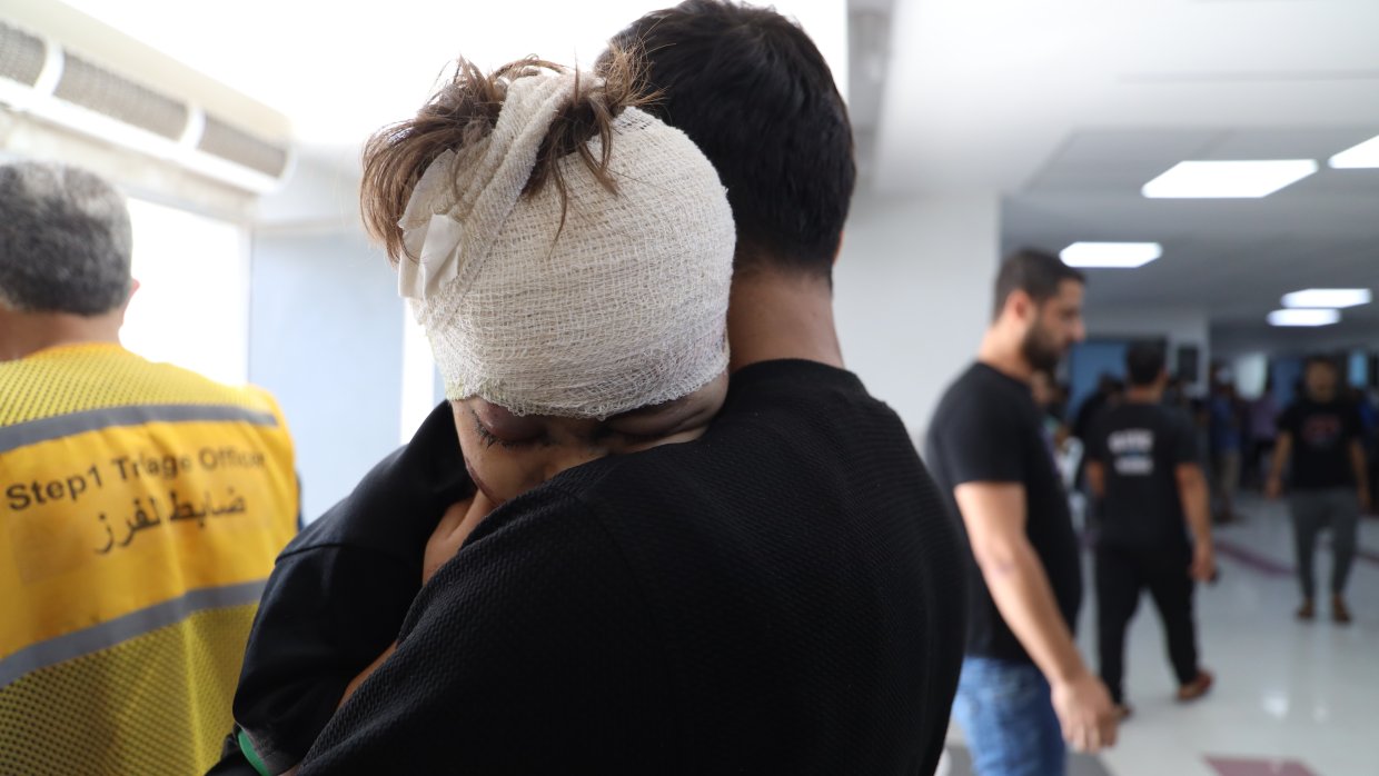 En man kramar en liten pojke med bandagerat huvud.