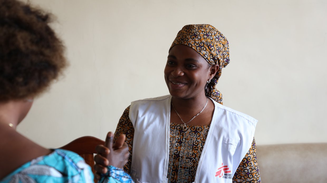 En kvinna med Läkare Utan Gränser-väst tar en kvinna med ryggen mot kameran i hand.