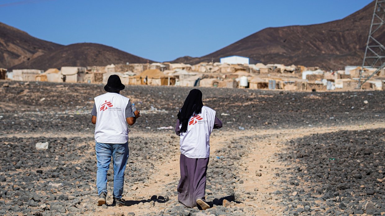 en man och en kvinna går mot en samling hus med ryggen mot kameran