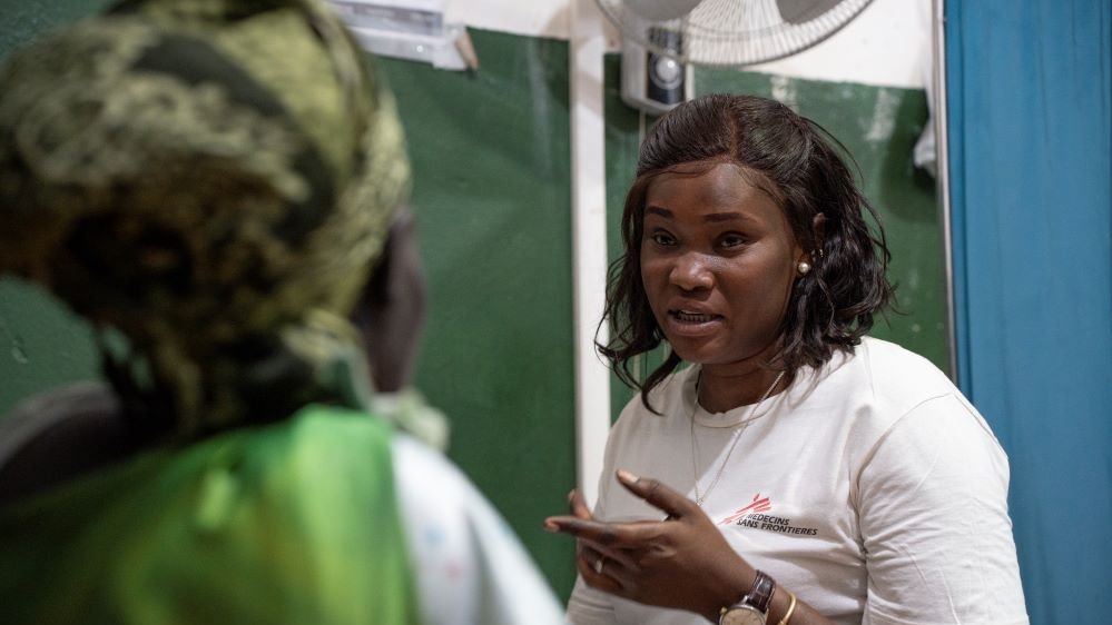 En kvinna i Läkare Utan Gränser-tröja sitter framför en kvinna i grönt med ryggen mot kameran.