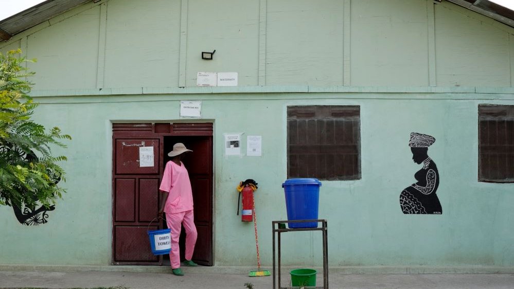 Ljusgrön byggnad med kvinna i rosa framför och ett konstverk på väggen.