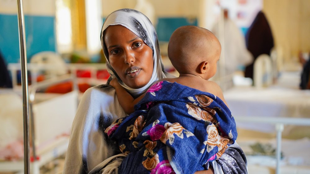 En kvinna tittar in i kameran. Hon håller ett barn över axeln.