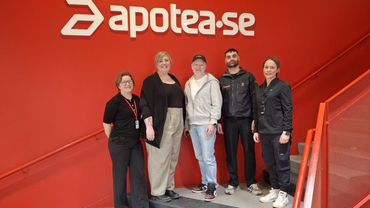 En grupp glada personer framför apoteas logga.