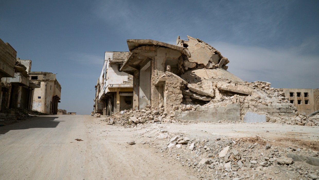 Förstörda byggnader i sandigt landskap.