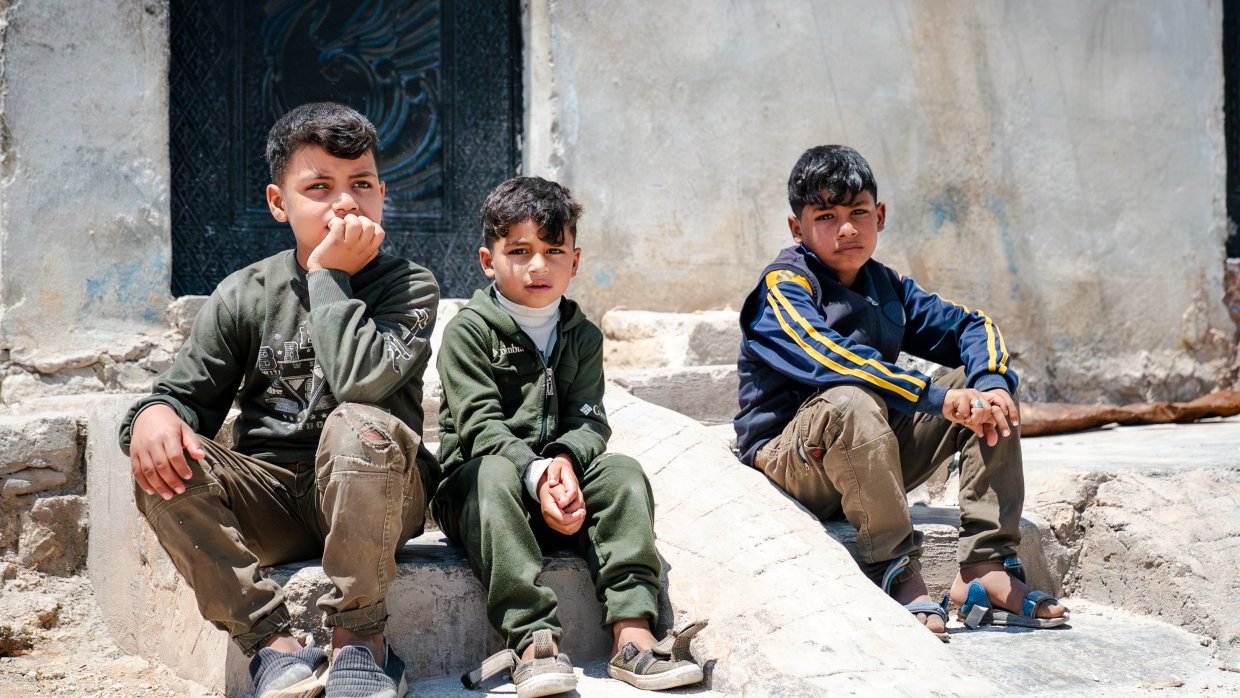 Tre barn som sitter utomhus på stenar/betongblock.