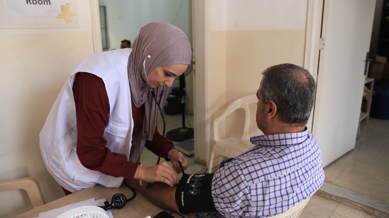En kvinna i Läkare Utan Gränser-väst undersöker en man i en stol.