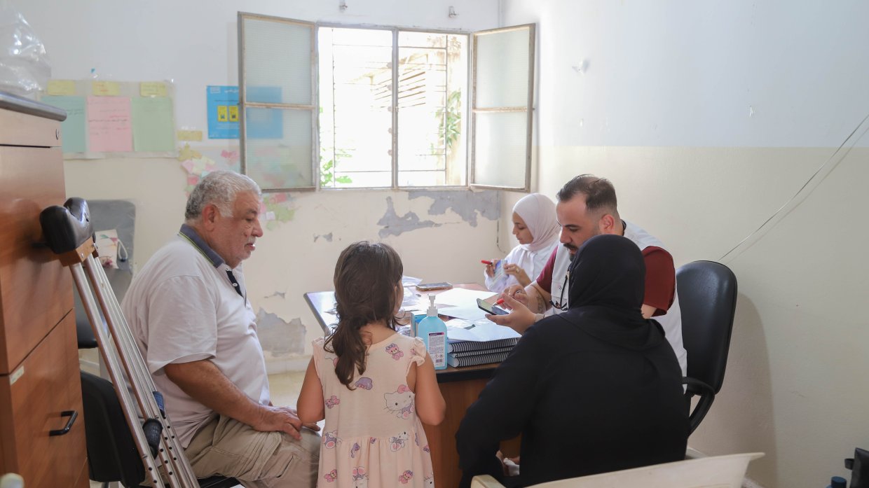 Fem människor runt ett bord, två i vit Läkare Utan Gränser-väst. 