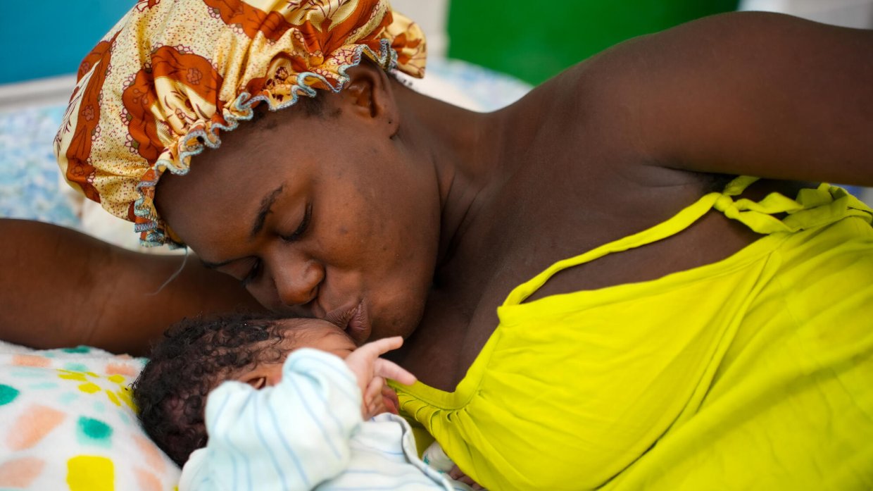 En mamma ligger ner i en säng och pussar sitt nyfödda barn.