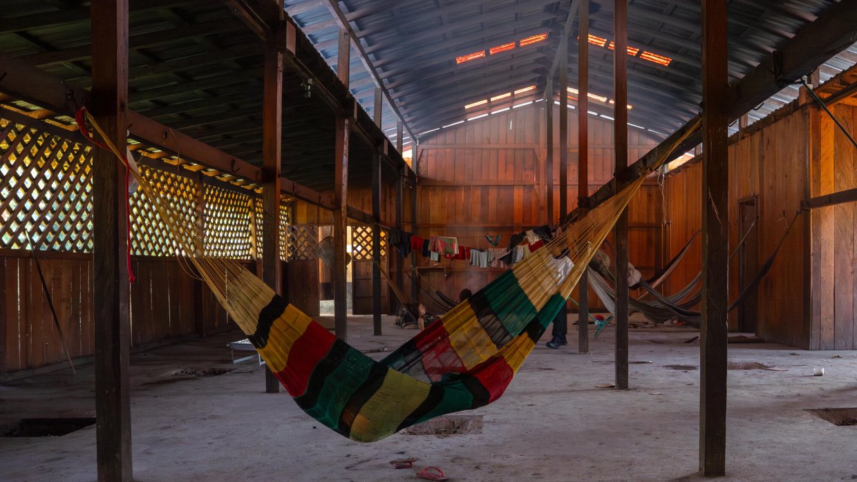 En färgglad hängmatta i typ hänger från träbjälkar inomhus i en avlång byggnad.
