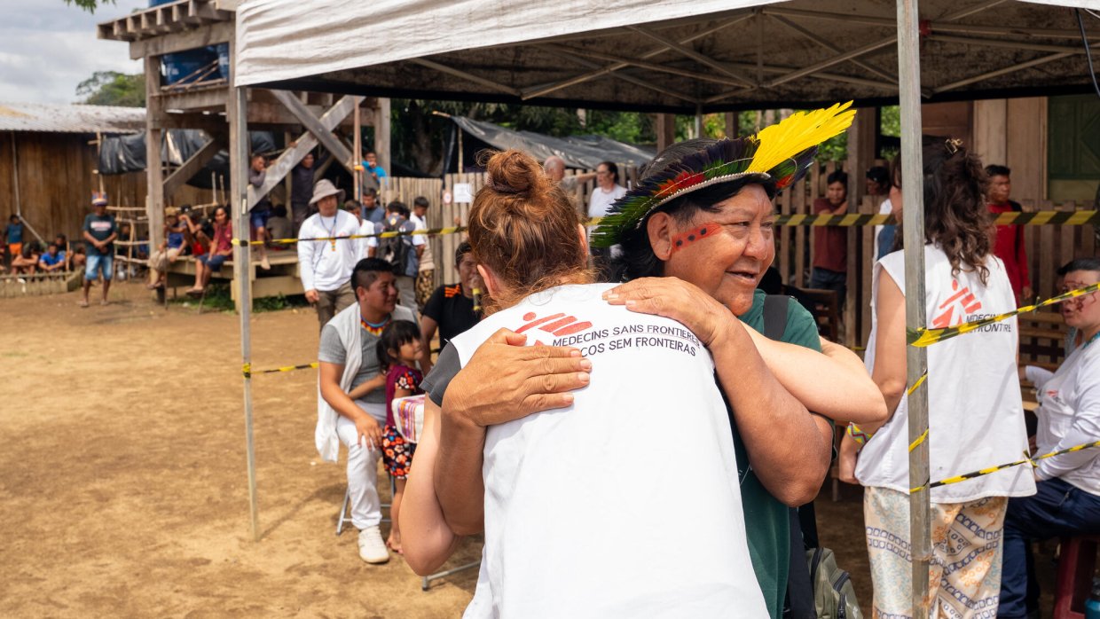 En person i Läkare Utan Gränser-väst kramar om en person med fjäderhuvudbonad och ansiktsmålning.