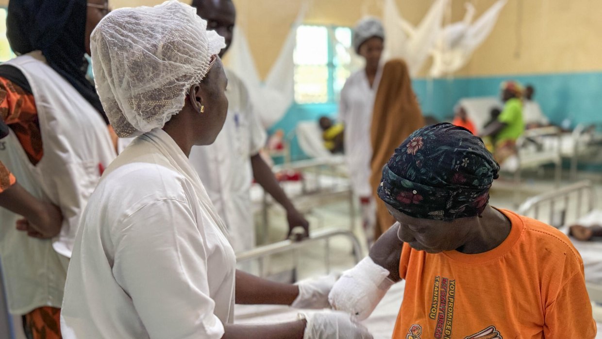 En kvinna i vita sjukhuskläder undersöker en kvinna med en bandagerad arm som slutar vid armbågen.