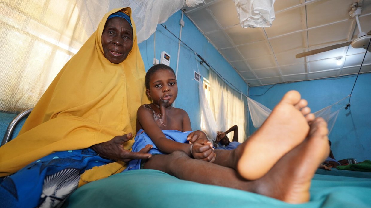 En kvinna och ett barn på en sjukhussäng, båda tittar in i kameran.