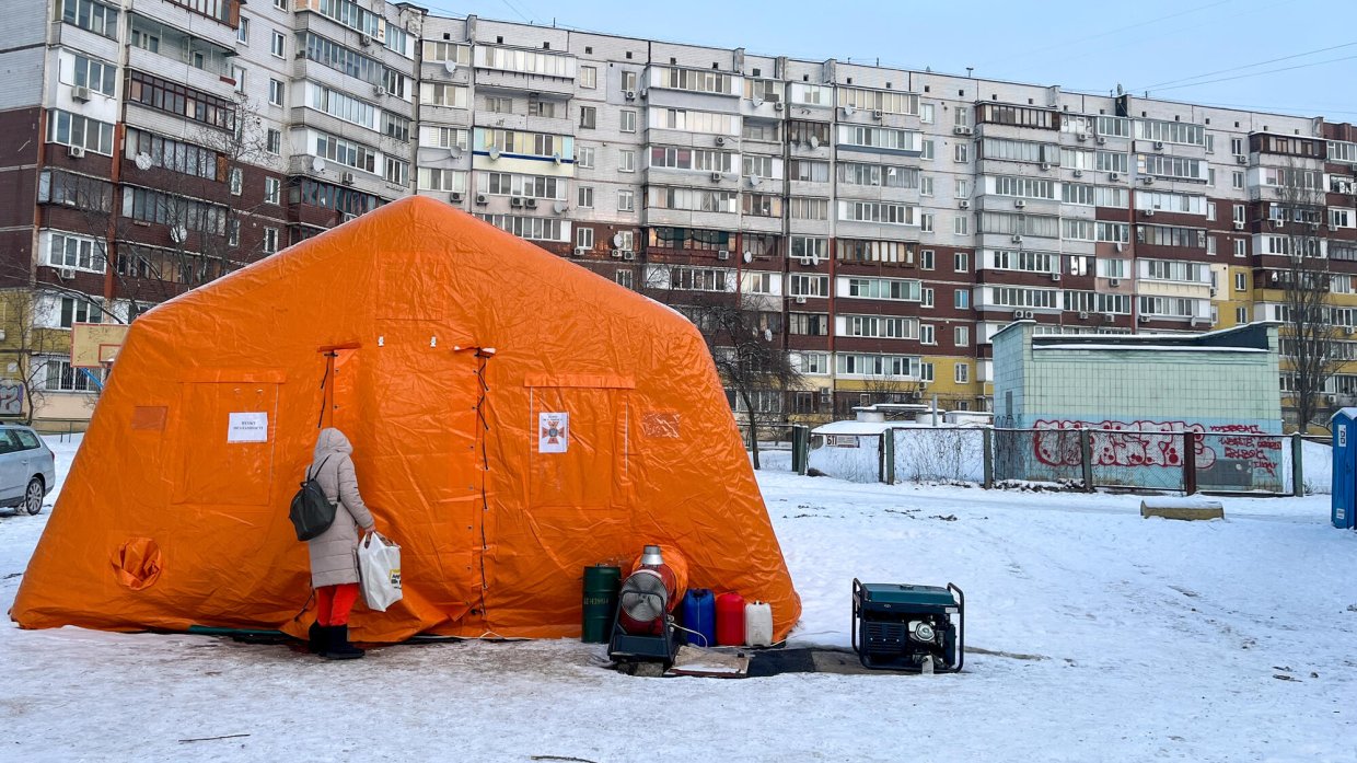 Ett orange tält framför lägenhetshus i snö.