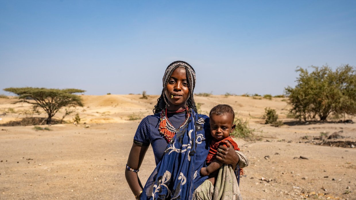 En kvinna med ett barn i famnen, i bakgrunden ett torrt landskap.