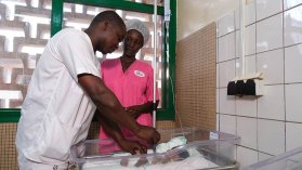 Två sjukhusanställda tar temperaturen på ett barn i en sjukhussäng.