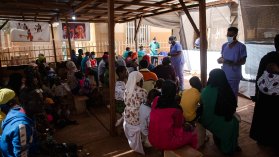 Ryggarna på ett tiotal människor som kollar mot en blåklädd anställd.