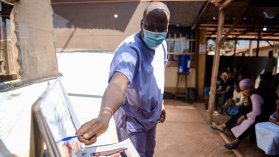 Man pekar mot en tavla med bilder, mittemot är det människor som sitter på stolar.