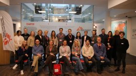 En stor grupp med människor från Postkodlotteriet och Läkare Utan Gränser står uppställda för gruppfoto i en kontorsmiljö