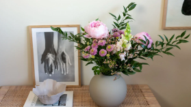 En yvig blombukett står i en grå vas på ett kaffebord bredvid tre staplade böcker