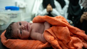 Nyfödd bebis ligger i en handduk och tittar in i kameran.