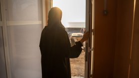 Kvinna står i solljuset vid dörröppning.