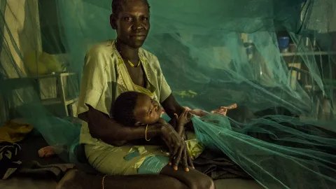 En mamma håller i sitt barn under ett myggnät