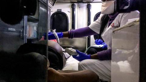 En kvinna gör ett ultraljud på en gravid kvinna som ligger på en bår i en ambulans.