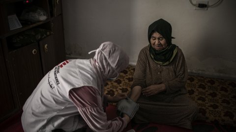 En sjuksköterska mäter blodtrycket på en äldre kvinna som sitter ner.