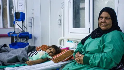 En kvinna sitter bredvid en sjukhussäng där det ligger en flicka, i Qayyrah, Irak,. 