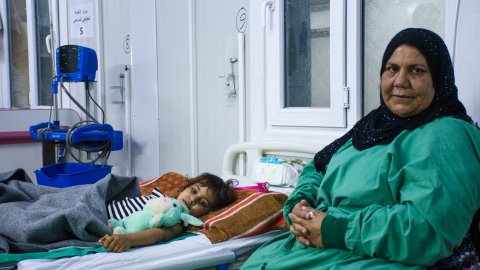 En kvinna sitter bredvid en sjukhussäng där det ligger en flicka, i Qayyrah, Irak,. 