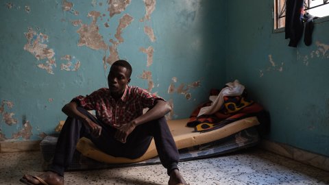 En man sitter på en madrass på golvet.