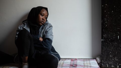 En flicka sitter på en madrass på golvet. 