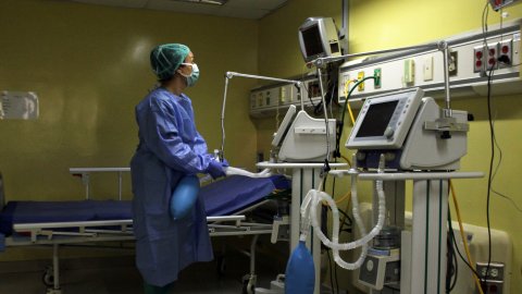 En medicinsk personal står iklädd skyddsutrustning och tittar på en monitor.