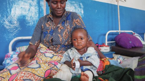 En kvinna sitter på en säng och håller om en liten pojke.