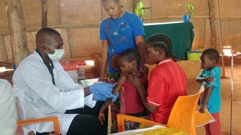 En sjukvårdsarbetare med en ansiktsmask och handskar som vaccinerar ett barn.