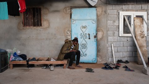 17-åriga Hassan från Sudan sitter på träbrits utanför ett hus i Libyen. 