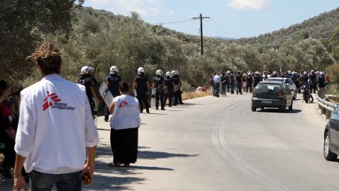 Personal från Läkare Utan Gränser tittar på när polisen för bort demonstranter utanför Moria, på den grekiska ön Lesbos.