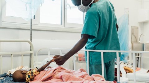 Tvååriga Sheku Kamara, som ligger på sängen på Läkare Utan Gränsers sjukhus i Kenema, Sierra Leone, håller en anställd i handen.