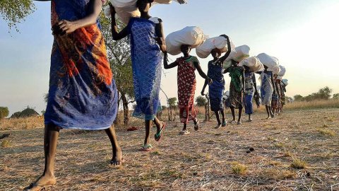 Kvinnor, boende i Riang, Sydsudam, går snett mot kameran på rad. De bär på förnödenheter som ska delas ut till boende i området.