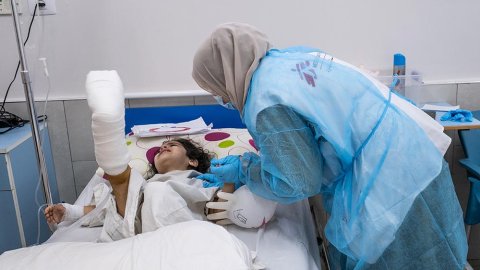 En sjuksköterska böjer sig över fyraåriga Halas säng på al-Awda sjukhus i norra Gaza, Palestina, för att trösta henne. Halas högra fot är gipsad.