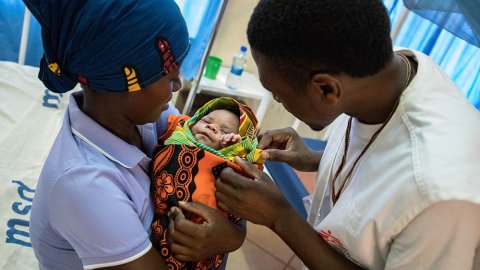 En anställd från Läkare Utan Gränser tittar till en nyfödd pojke på sjukhuset i Nduta flyktingläger i Tanzania. Pojken är invirad i en filt och hans mamma håller hon tätt intill sig.