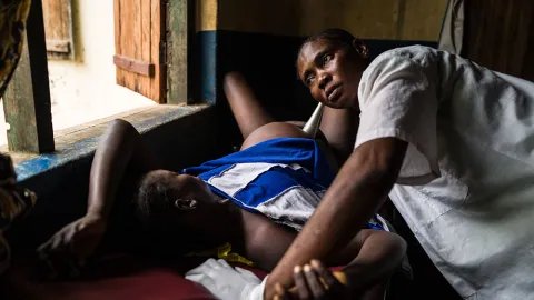 Octavia Braza, som bor i Nzacko, Centralafrikanska republiken, ligger på en brits i färd med att föda sitt sjunde barn. Barnmorskan Sylvia lyssnar på bebisens hjärtslag.