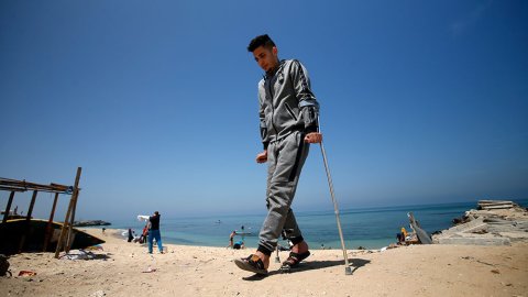 En ung man går på kryckor på en strand i Gaza, Palestina.