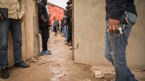 Människor står vid en dörröppning i förvaret Dahr-el-Jebel i Libyen. Det är lerigt på marken.