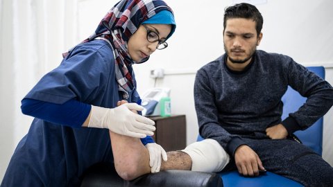 Fysioterapeuten Sabrine Wadi på al-Awda-sjukhuset i Gaza tittar till en patients fot. Patienten sitter på en sjukhusbrits.